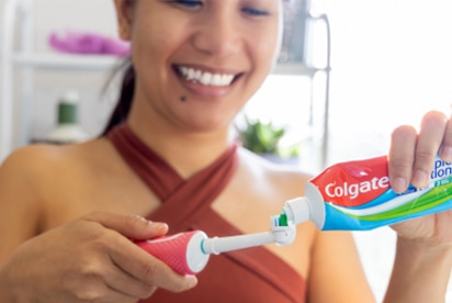Mosolygó nő, aki éppen Colgate fogkrémet tesz a fogkefére a fürdőszobában.